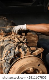 Close up of a mechanic's gloved hands using a spanner to adjust the gear shift linkages and fix a sensor on a heavy vehicle transmission gearbox in a garage workshop.