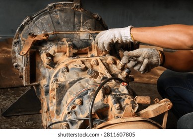 Close up of a mechanic's gloved hands using a spanner to adjust the gear shift linkages and fix a sensor on a heavy vehicle transmission gearbox in a garage workshop.