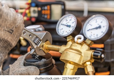 Close up of mechanic's hand tightening the valve with a wrench. Two gauges visible on the appliance. Blurred background.  - Shutterstock ID 2257469917
