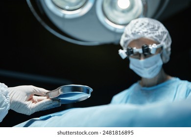 Close up of medical assistant handing dish to female surgeon in operating room with blurred background copy space - Powered by Shutterstock