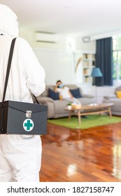 Close up medical staff in personal protective equipment PPE suit with background of asian woman with face mask waiting in living room of apartment .Delivery coronavirus covid-19 test at home concept.
