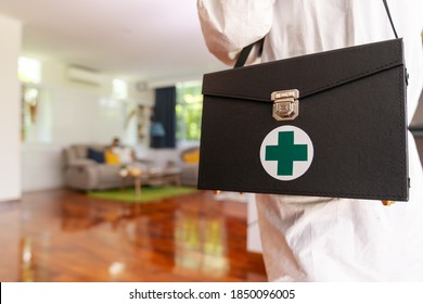 Close up medical staff in personal protective equipment PPE suit with background of asian woman with face mask waiting in living room of apartment .Delivery coronavirus covid-19 test at home concept.