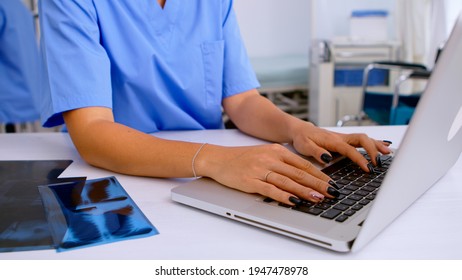 Close Up Of Medical Woman Nurse Writing Results Of Patient Radiography, Typing On Laptop Sitting In Hospital. Radiologist In Medical Uniform Looking At X-ray, Examination, Bone, Analyze, Diagnosis.