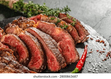 Close up of medium rare sliced tomahawk steak with sea salt, thyme and chili pepper. Juicy grilled beef with visible marbling and texture.