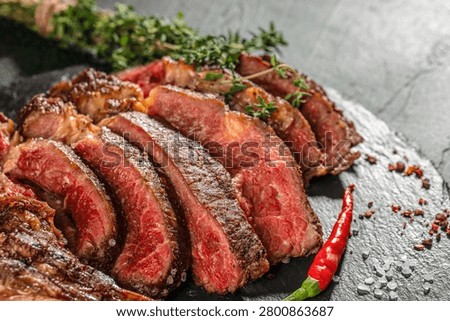 Close up of medium rare sliced tomahawk steak with sea salt, thyme and chili pepper. Juicy grilled beef with visible marbling and texture.