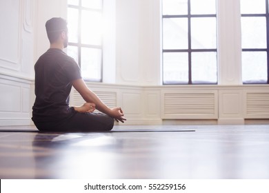 Close up men hands, back view. Young men do yoga indoors on black mat. Guy exercising yoga with a black background in gym. Young men meditating in lotus posture closeup.