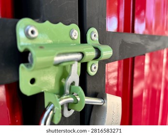 Close Up of Metal Padlock Securing a Red Gate with Green Latch