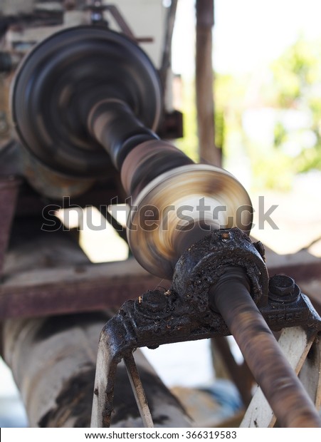 close up of a metal steel drive shaft of a water\
pump on a large size ball bearing support and universal joint with\
dark dirty grease on running working showing motion blur on the\
machine moving parts