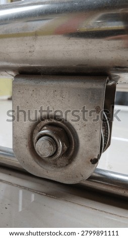 Close up of a metallic sliding gate roller wheel attached with a bolt and nut structure on a stainless steel rail pipe.