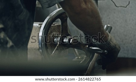 Close up of a metalworker's hands skillfully operating a lathe machine, turning and shaping metal components in a workshop environment, showcasing precision and craftsmanship in metal production