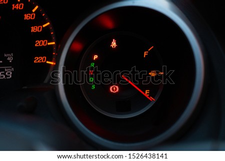 Close up of meter panel with the needle pointing at E on black blackground, car has run out of gas