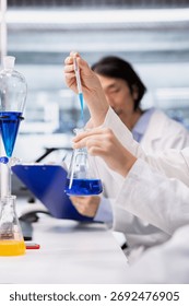 Close up of microbiologists brainstorming, using pipette to dispense reagent into test tube at laboratory bench. Modern research facility coworkers do pipetting procedure with dropper