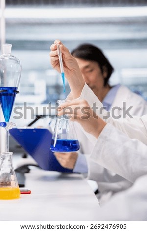Close up of microbiologists brainstorming, using pipette to dispense reagent into test tube at laboratory bench. Modern research facility coworkers do pipetting procedure with dropper