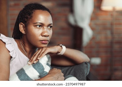 Close up of a mid adult black woman thinking of something while sitting on sofa at home - Powered by Shutterstock