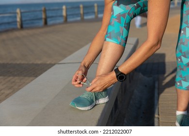 Close Up Mid Section Of A Mature Middle Aged Caucasian Woman Working Out On A Promenade, Bending Over, Tying Her Shoe Laces