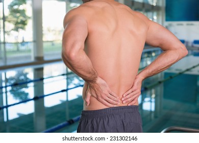 Close up mid section of a shirtless fit swimmer with back ache by the pool - Powered by Shutterstock