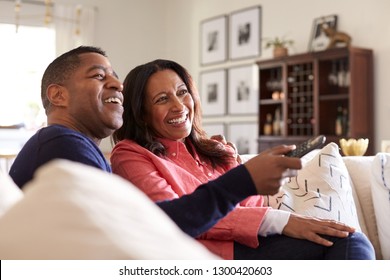 Close Up Of Middle Aged African American Couple Sitting On The Sofa In Their Living Room Using Remote And Watching TV, Laughing, Close Up