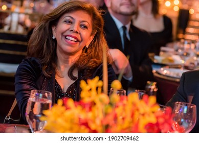 A close up of a middle aged african american woman laughing at a black tie gala. There is a colorful bouquet of flowers in the foreground.