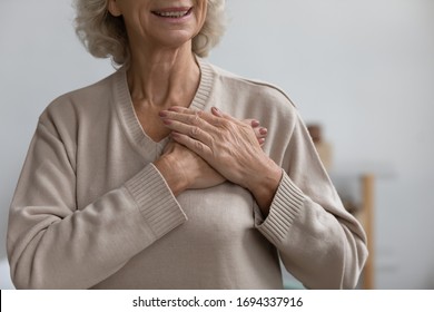 Close Up Middle Aged Happy Woman Thanking God With Folded Hands On Heart, Grateful Sincere Smiling Senior Older Grandmother Holding Hands On Chest Feeling Excited By Good News, Believe Faith Concept.