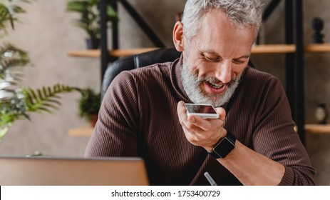 Close Up Of Middle Aged Man Writing Notes In Notepad While Talking By Speakerphone From Workspace