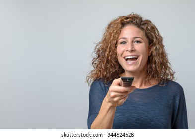 Close up Middle Aged Woman in Casual Pullover Holding Remote Control While Looking at the Camera, Isolated on Gray Wall Background.
