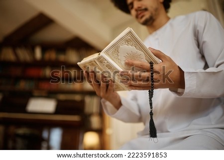 Close up of Middle Eastern man reading from Koran while using misbaha beads and praying at home