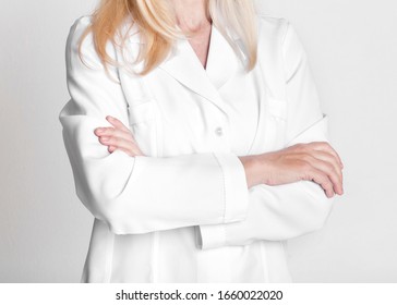 Close Up Of Middle-Aged Woman Doctor Wearing White Uniform, Standing With Folded Arms On Grey Studio Wall