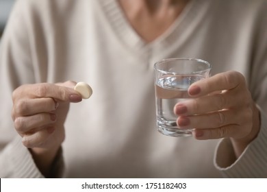 Close up of middle-aged woman hold tablet and glass of water taking daily dose of vitamins or supplements, mature female having medicines pills at home, elderly healthcare, medication concept - Shutterstock ID 1751182403