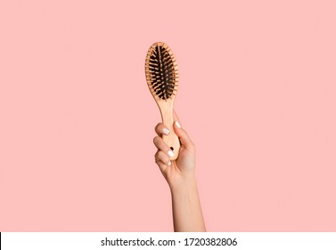 Close up of millennial girl holding wooden hairbrush on pink background