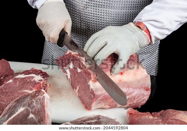 Close up\
of minced meat pieces and butcher\'s male hands in special gloves\
cutting with knife. Meat pork or beef on the butcher\'s table.\
Worker in white uniform and special steel\
apron.
