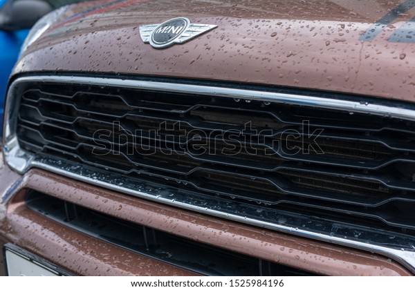 Close Up of mini\
cooper logo with raindrops and front grille car mini cooper on\
braun car parked in\
street
