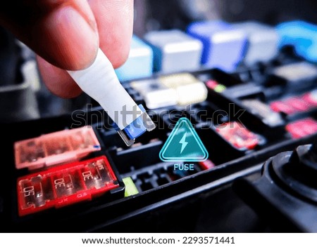 Close up of mini fuse for electric car system with a voltage caution symbol and fuse box on blurred background, automotive parts concept.