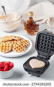A close up of a mini waffle maker with batter to make heart waffles.