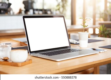 Close Up Minimalist Shot Of Generic Laptop Computer And Working Accessories Resting On Wooden Table Against Blurred Background Of Cafeteria. Workplace Of Unknown Freelancer. Selective Focus