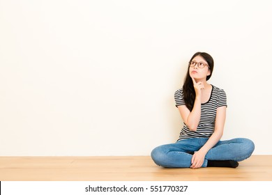 Close Up Of A Mixed Race Asian Woman Thinking About Question Wearing T-shirt Top Sitting Over Blank Copy Space White Wall Background.