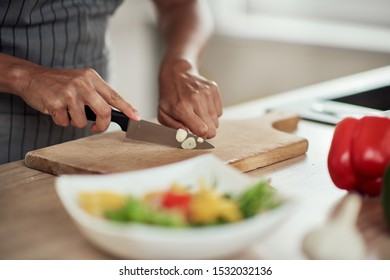 Close up of mixed race woman in apron standing in domestic kitchen and cutting garlic. - Powered by Shutterstock