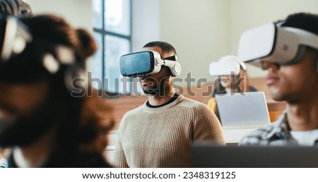 Close up of mixed-races males and female students in VR glasses listening to lection at college and rising hands to answer. Hi-tech study. Multiethnic young people having virtual reality education.