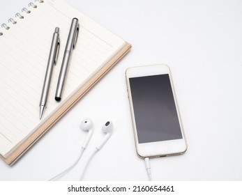 Close Up Mobile Phone With Ear Phone And Pen With Diary Book On Table