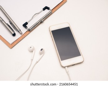 Close Up Mobile Phone With Ear Phone And Wood Board Document On Table