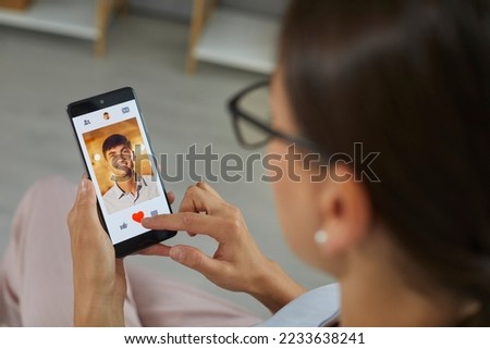 Close up of mobile phone with open dating application in hands of woman looking for relationship. Woman scrolling through profiles on dating site clicks red heart as sign of man's liking.