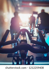 Close Up Modern Bike With Blurred Row Of Man And Woman Exercise Bikes. Fitness Cycling Indoor Concept.