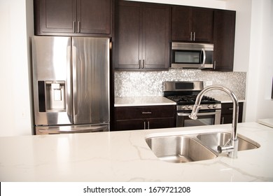 Close Up Of A Modern Kitchen, With A Sink On A Quartz Counter Top And Dark Wooden Shelves. Focus On The Silver Faucet.