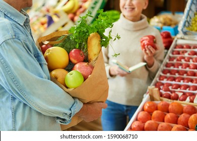 Close up of modern senior couple choosing fresh vegetables while enjoying shopping in farmers market, focus on paper bag with groceries in foreground, copy space - Powered by Shutterstock