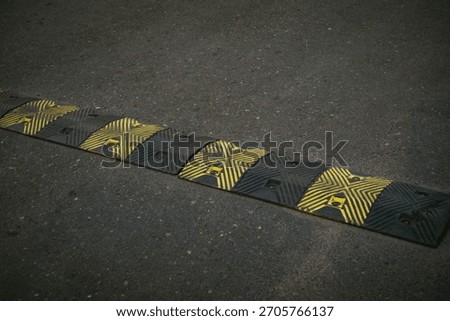 Close up of a modular rubber speed bump with black and yellow warning stripes installed on an asphalt road. Strong texture and diagonal lines for background use. Foto detail polisi tidur