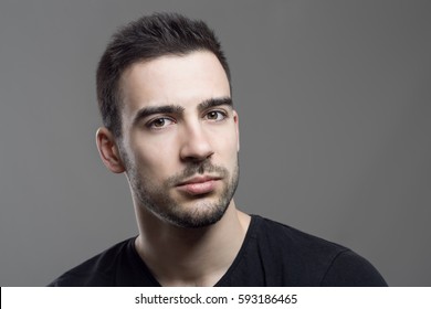 Close Up Moody Portrait Of Skeptical Stubble Man Looking At Camera Over Dark Gray Studio Background.