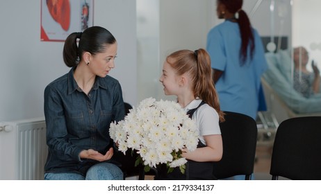 Close Up Of Mother And Child In Waiting Area Preparing To Visit Patient, Having Bouquet Of Flowers. Woman With Kid Waiting To See Ill Person In Hospital Ward At Medical Facility. Waiting Room