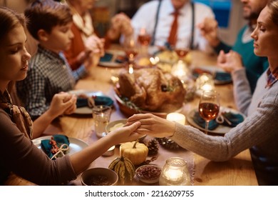 Close Up Of Mother And Daughter Holding Hands During Family Prayer On Thanksgiving At Dining Table.