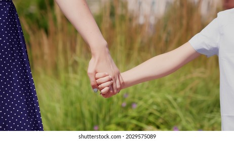 Close Up Of Mother Holding Hand Of Son On Spring Day Outdoors. Cropped Shot Of Young Woman And Little Child Hold Hands In Park