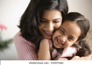 close-up da mãe abraçando a filha, a menina está sorrindo para a câmera