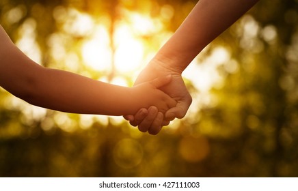 Close up of mother or older sister and a child hands at the sunset with copy space